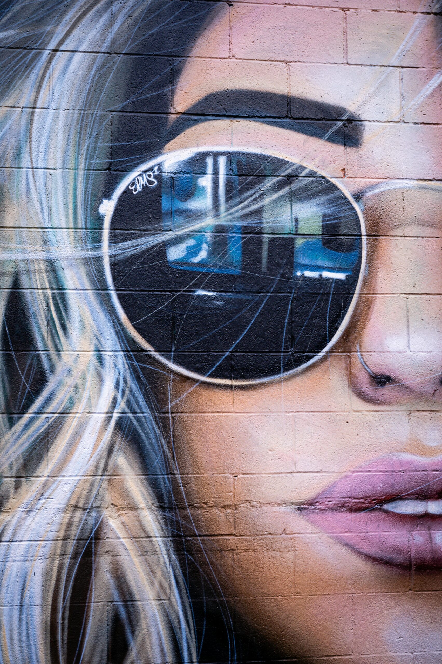 Close-up of a colorful mural depicting a woman wearing reflective sunglasses on a brick wall.